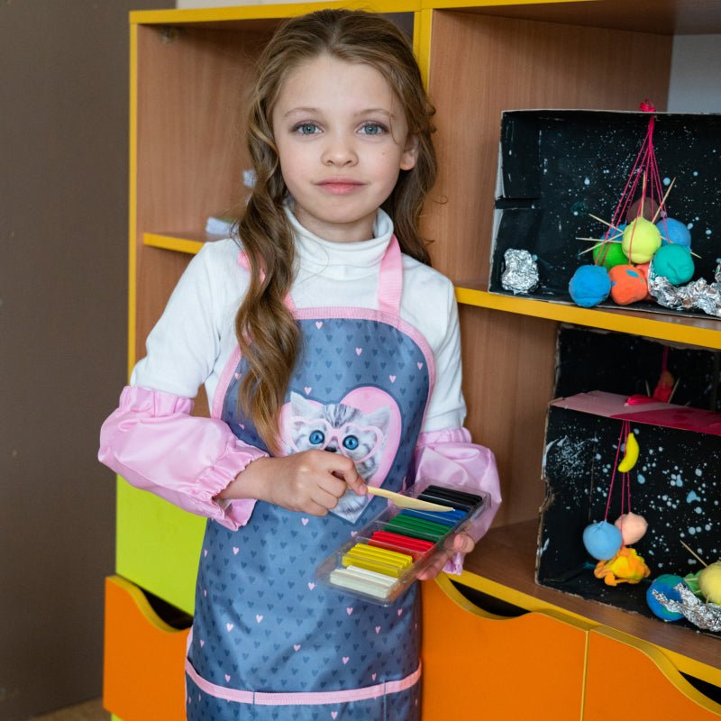 Dziewczynka w fartuszku plastycznym trzyma kredki, szkolny fartuszek ochronny do malowania dla dzieci